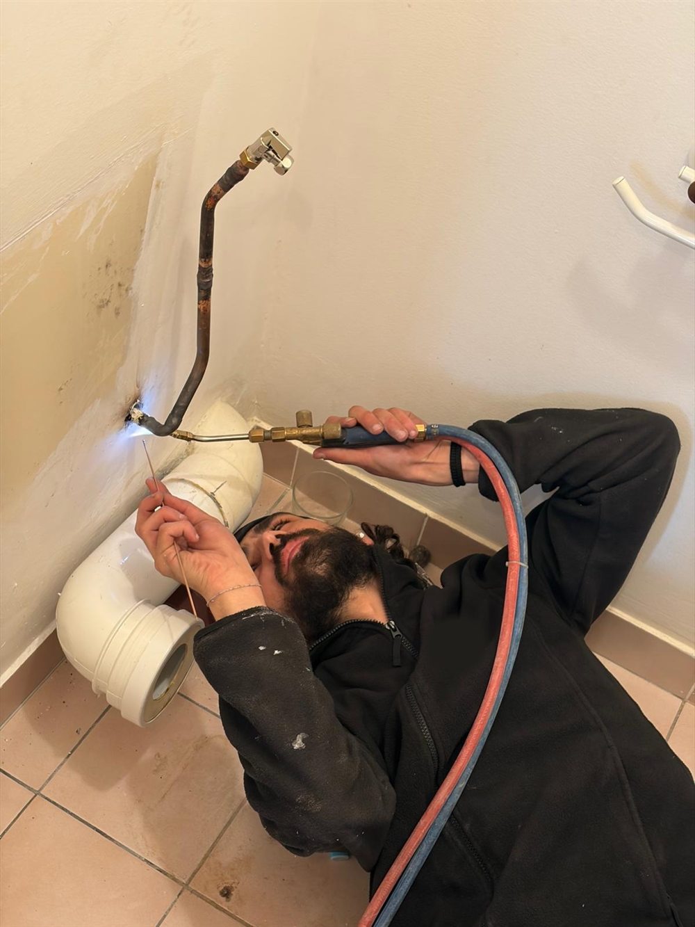 Le plombier de SAD Plomberie soude un tuyau en cuivre au chalumeau, allongé au sol d'un WC en chantier